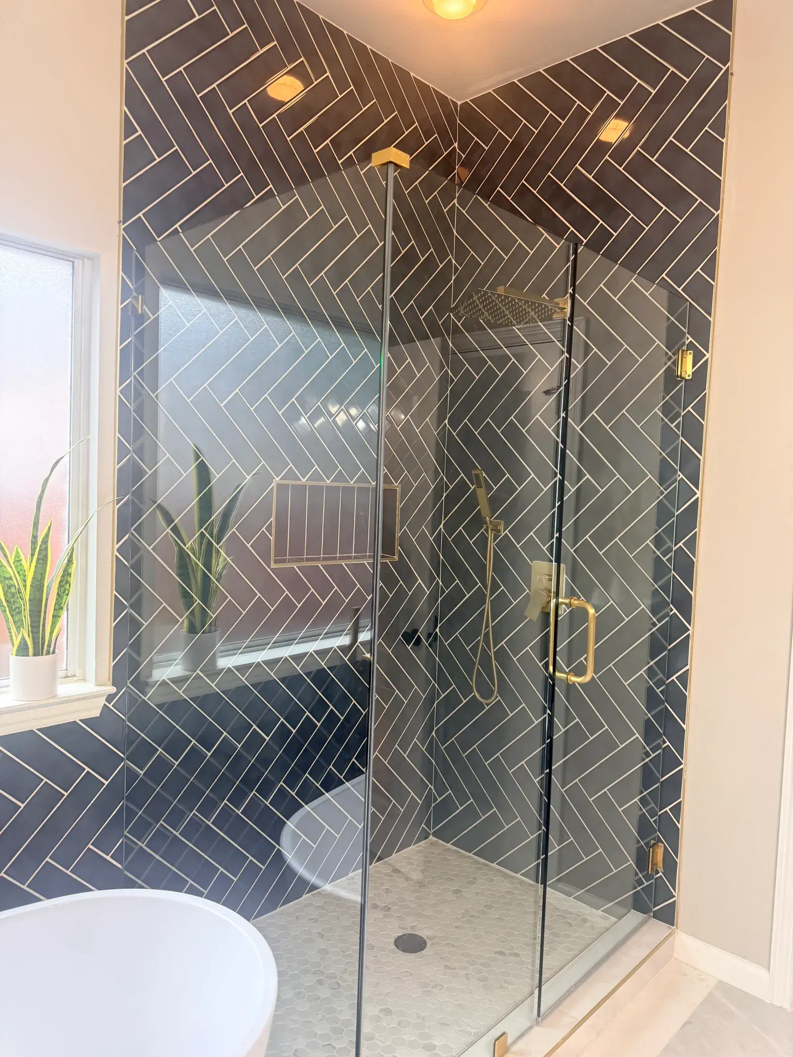 Shower in charcoal herringbone tile behind frameless glass with brass hardware