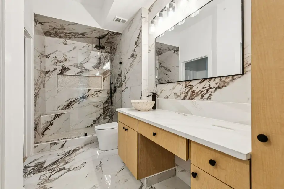 Bath with bookmatched marble-look slab walls and an oak vanity