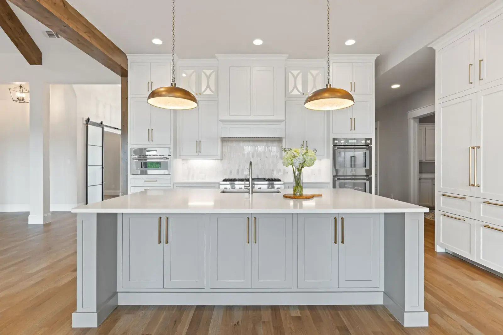 Kitchen with white shaker cabinets, brass pulls, a white island and marble-look backsplash under brass pendants