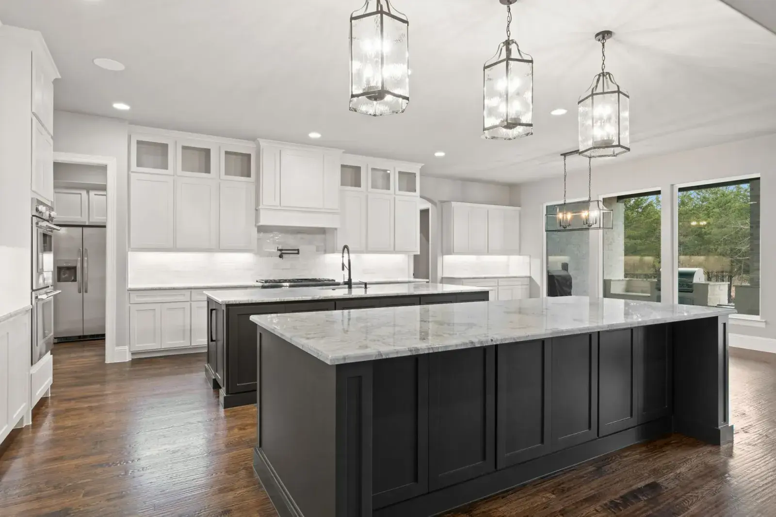 Kitchen with white perimeter cabinets, a dark island under a white veined top, and three lantern pendants